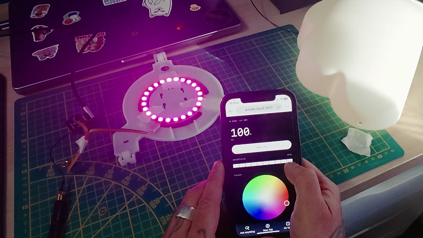 The ring lit magenta on the bench while a phone shows the lamp's own control page with a colour wheel